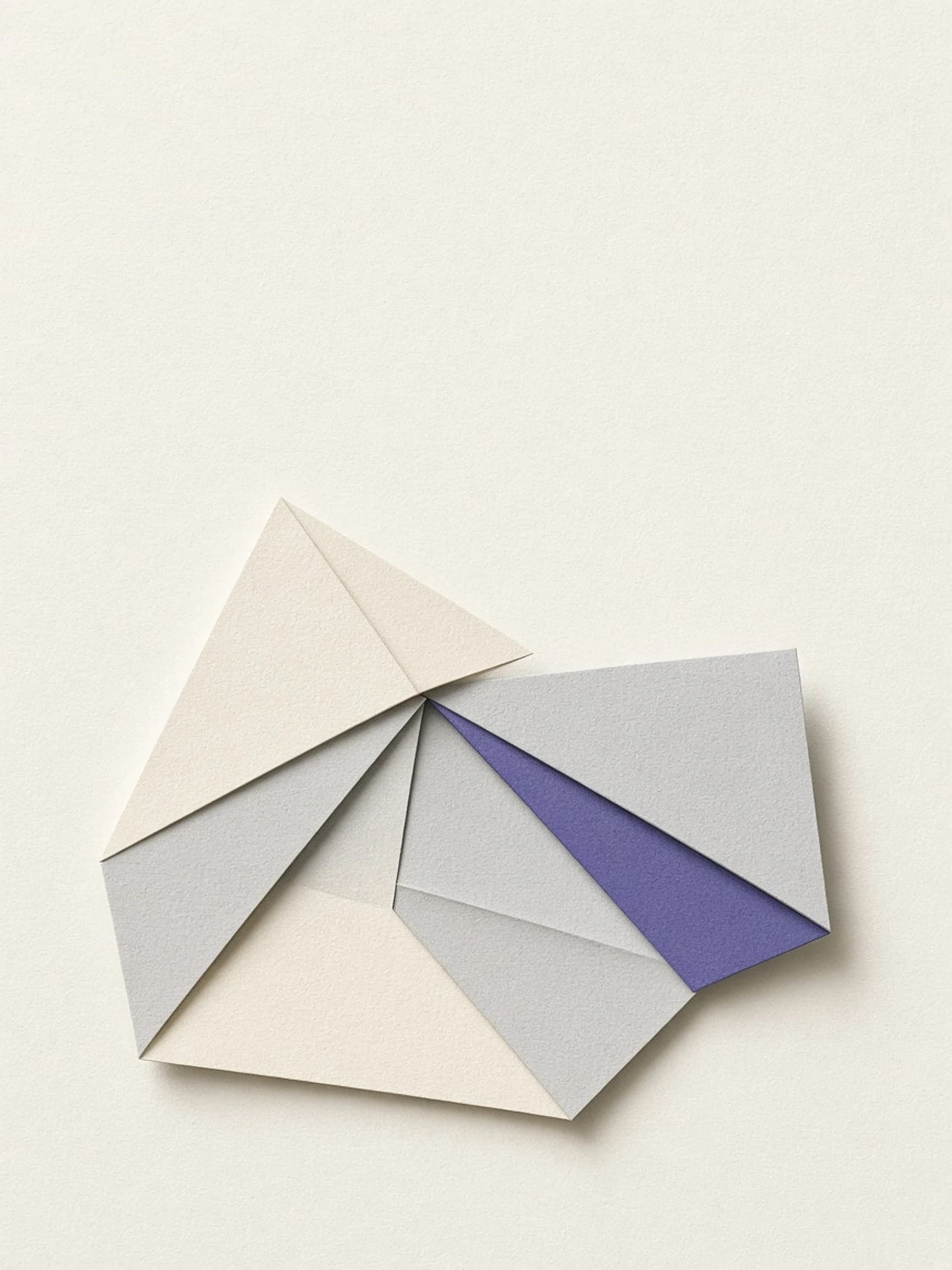 Ivory and grey paper folded into geometric shapes, with one violet facet